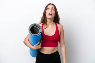 Young sport caucasian woman going to yoga classes while holding a mat isolated on white background looking up and with surprised expression