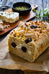 Loaf of village, fresh bread with feta and black olives on wooden table
