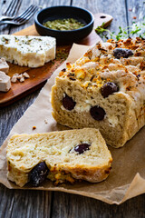 Loaf of village, fresh bread with feta and black olives on wooden table

