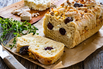 Loaf of village, fresh bread with feta and black olives on wooden table
