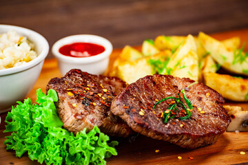 Barbecued meat, french fries and vegetables on wooden board 