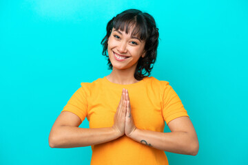 Young Argentinian woman isolated on blue background keeps palm together. Person asks for something
