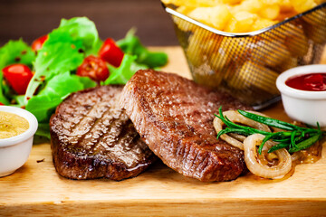 Barbecued meat, french fries, asparagus and vegetables on wooden board 