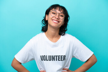 Young volunteer Argentinian woman isolated on blue background posing with arms at hip and smiling