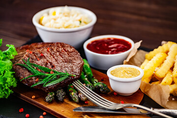 Barbecued meat, french fries, asparagus and vegetables on wooden board 