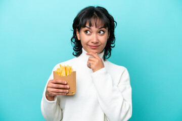 Young Argentinian woman holding fried chips isolated on blue background looking up while smiling
