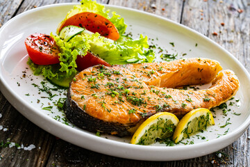 Fried salmon steak and fresh vegetable salad served on wooden table
