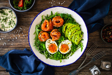 Salmon salad - smoked salmon, hard boiled eggs, avocado and leafy greens on wooden table

