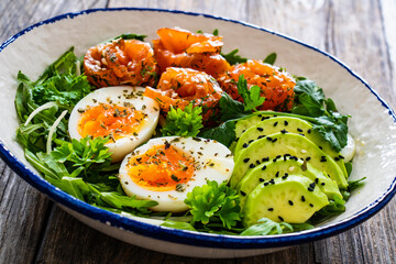 Salmon salad - smoked salmon, hard boiled eggs, avocado and leafy greens on wooden table
