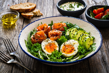 Salmon salad - smoked salmon, hard boiled eggs, avocado and leafy greens on wooden table
