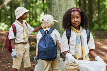 Waist up portrait of cute black girl as scout helping clean forest and holding trash bag, copy space