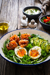 Salmon salad - smoked salmon, hard boiled eggs, avocado and leafy greens on wooden table
