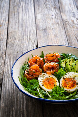 Salmon salad - smoked salmon, hard boiled eggs, avocado and leafy greens on wooden table

