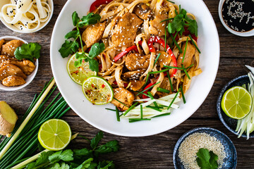Asian food - chicken nuggets, noodles and stir fried vegetables on wooden table
