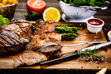 Barbecued meat, french fries, asparagus and vegetables on wooden board 
