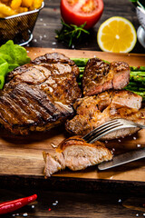 Barbecued meat, french fries, asparagus and vegetables on wooden board 
