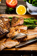 Barbecued meat, french fries, asparagus and vegetables on wooden board 
