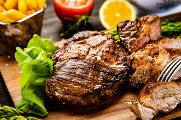 Barbecued meat, french fries, asparagus and vegetables on wooden board 
