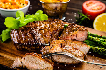 Barbecued meat, french fries, asparagus and vegetables on wooden board 

