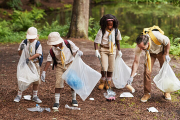 Full length diverse group of scouts picking up trash in forest during eco awareness field trip