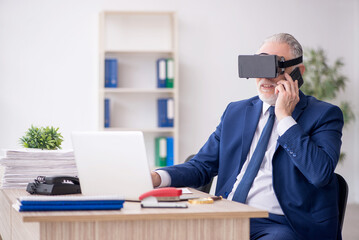 Naklejka premium Old male employee wearing virtual glasses at workplace
