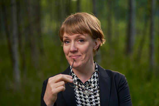 portrait of a female buissness woman holding her glasses to her mouth and smiling