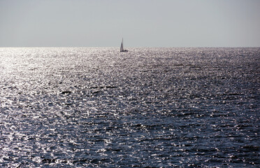 Shiny sea horizon with sailing yacht and silver shining waves