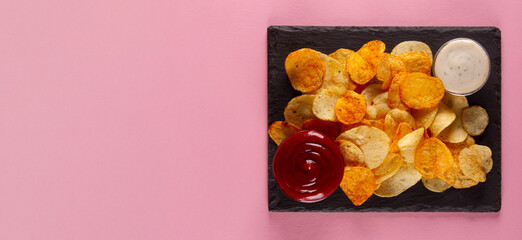 Perfectly salted and crispy potato chips with creamy white and savory red dip on pink background