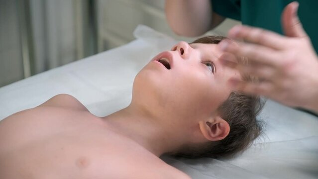 Session of craniosacral therapy, cure of teen boy's jaw by a doctor therapist. Craniosacral therapist touches the boy's cheeks and checks the correctness of the jaws at the hospital.