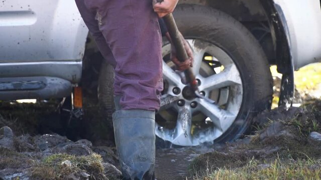 Slow motion view person cleaning up of stuck car wheel from mud