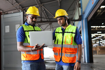 Group of warehouse workers with hardhats and reflective jackets using computer, walkie talkie radio and cardboard controlling stock and inventory in retail warehouse logistics, distribution center