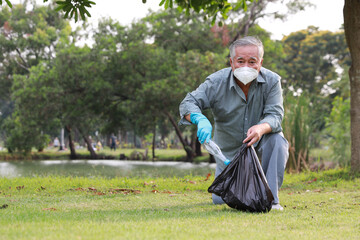 volunteer tourist asian senior man cleaning up garbage and plastic debris on dirty park by collecting them into big black bag