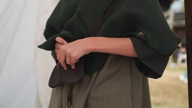 Young woman hides small glass bottle with witchcraft potion in purse. Medieval woman uses magic power secretly on blurred background closeup