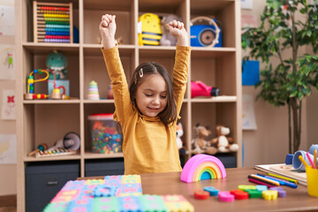 Adorable hispanic girl playing with construction blocks with winner expression at kindergarten