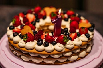 Closeup of the first birthday cake decorated with strawberries and blueberries with a lit candle