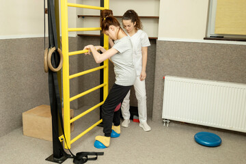 Disabled Teenage Girl With Doctor Does Physical Exercises In Rehabilitation Room. Child With Special Needs. Rehabilitation. Cerebral Palsy. Motor Disorder. Horizontal plane. - obrazy, fototapety, plakaty