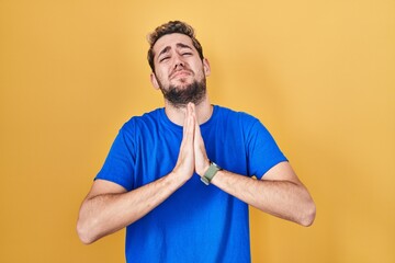 Hispanic man with beard standing over yellow background begging and praying with hands together with hope expression on face very emotional and worried. begging.