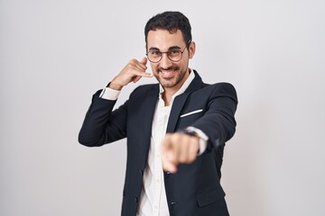 Handsome business hispanic man standing over white background smiling doing talking on the telephone gesture and pointing to you. call me.