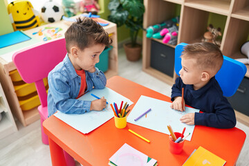 Adorable boys preschool students sitting on table drawing on paper at kindergarten