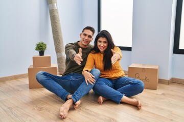Young couple sitting on the floor at new home smiling friendly offering handshake as greeting and welcoming. successful business.