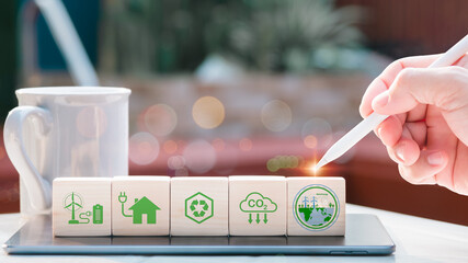 Concept of net zero and carbon neutrality. Hand places wooden cubes with the netzero icons for waste recycling, green production, reducing carbon emissions, and renewable energy.background green