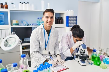 Man and woman scientists partners using microscope working at laboratory