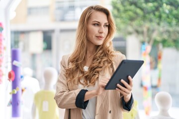 Fototapeta premium Young blonde woman shop assistant using touchpad working at clothing store