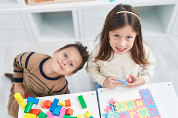 Fototapeta premium Adorable boy and girl playing with construction blocks and vocabulary puzzle at kindergarten