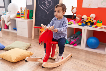 Adorable hispanic boy playing with reindeer rocking at kindergarten