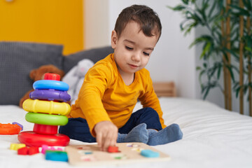 Adorable hispanic boy playing with maths puzzle game sitting on bed at bedroom