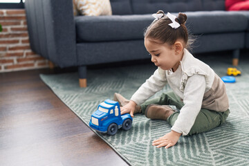 Adorable hispanic girl playing with car toy sitting on floor at home
