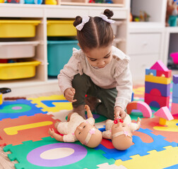 Adorable hispanic girl sitting on floor playing with baby doll at kindergarten