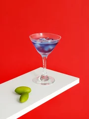Poster Blue Moon Cocktail glass and olives on white surface isolated on red background © Jingluo/Wirestock Creators