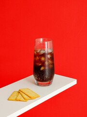 Cold carbonated drink with ice cubes and Cracker Biscuit isolated on red background